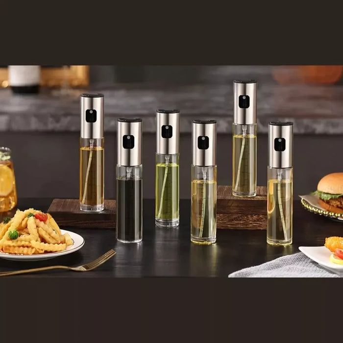 Seis pulverizadores de óleo inox sobre mesa de cozinha, próximos a batatas fritas e hambúrguer.