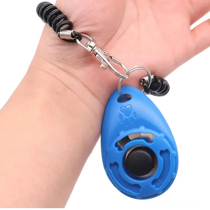 Mão segurando clicker azul para adestramento de cães com pulseira espiral preta.